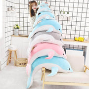 young woman playing with big, medium, and small dolphin plushie pillows in blue, pink, and gray