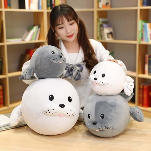 young woman holding cute kawaii round chonky seal plushies in gray and white