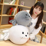 young woman holding cute kawaii round chonky seal plushies in gray and white