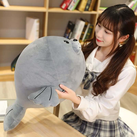 young woman playing with cute kawaii round chonky seal plushie in gray