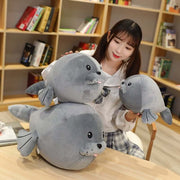 young woman playing with cute kawaii round chonky seal plushies in gray